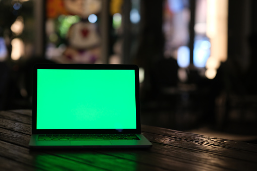 front view of green screen laptop computer at dark night. Defocused lights background