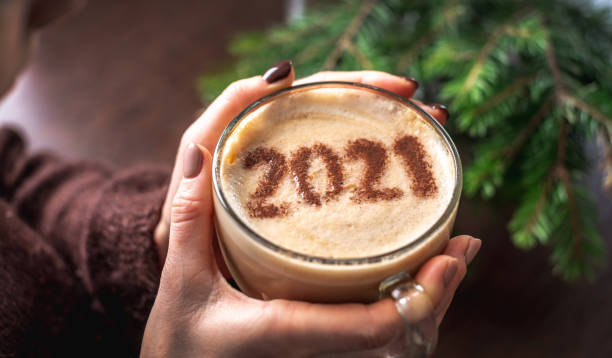 les mains des femmes tiennent une tasse de café transparente. il ya des chiffres 2021 sur la mousse de lait de cannelle. concept d’une nouvelle année - foamed milk photos et images de collection