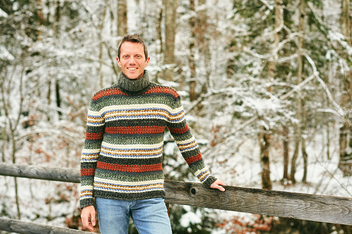 Outdoor winter portrait of middle age man in snowy forest, wearing warm knitted pullover