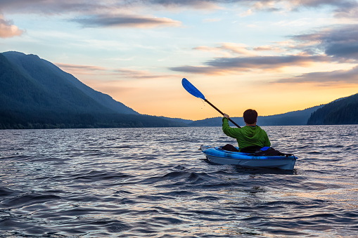 Beautiful View of Person Kayaking on Scenic Lake at Sunset surrounded by Mountains in Canadian Nature. Taken in Golden Ears Provincial Park, near Vancouver, British Columbia, Canada.