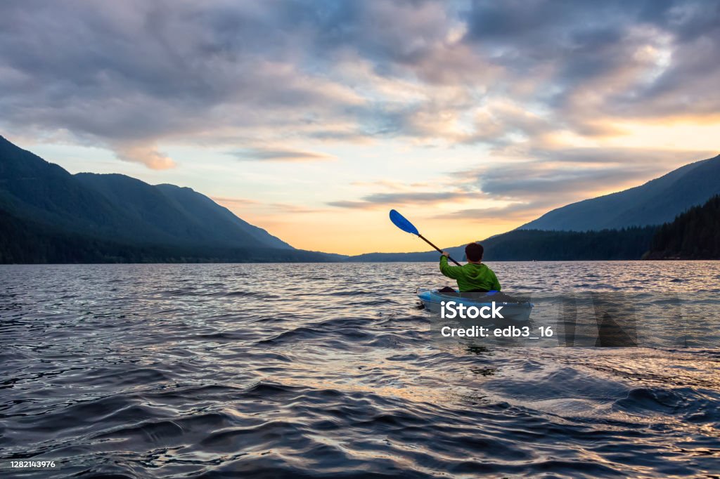 Beautiful View of Person Kayaking on Scenic Lake at Sunset Beautiful View of Person Kayaking on Scenic Lake at Sunset surrounded by Mountains in Canadian Nature. Taken in Golden Ears Provincial Park, near Vancouver, British Columbia, Canada. Golden Ears Provincial Park Stock Photo