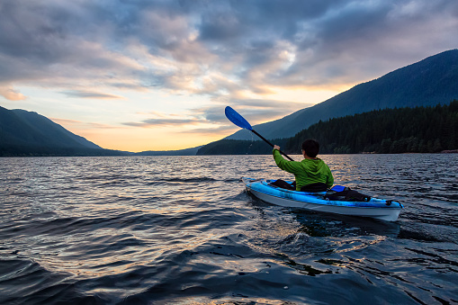 Beautiful View of Person Kayaking on Scenic Lake at Sunset surrounded by Mountains in Canadian Nature. Taken in Golden Ears Provincial Park, near Vancouver, British Columbia, Canada.