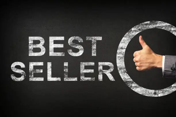 Photo of Hand of a businessman showing thumbs up for the phrase BEST SELLER written on a blackboard