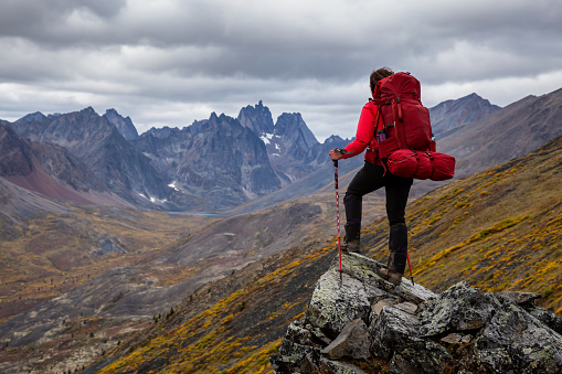 Woman Standing on Rocks looking at Scenic Mountain Peaks and Valley during Fall in Canadian Nature. Taken in Tombstone Territorial Park, Yukon, Canada.