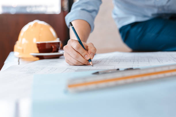istock engineers holding a pen pointing to a building and  drawing outlay construction plan as guide for builders with details. Engineer design and writing blueprint. 1282149585