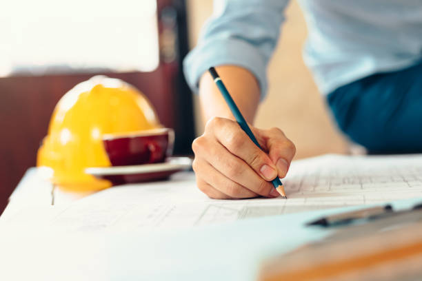 istock engineers holding a pen pointing to a building and  drawing outlay construction plan as guide for builders with details. Engineer design and writing blueprint. 1282149603