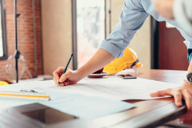 istock engineers holding a pen pointing to a building and  drawing outlay construction plan as guide for builders with details 1282149616