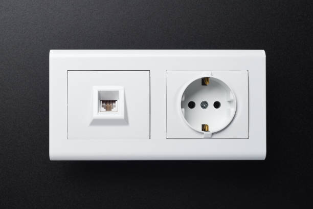 istock An electric wall socket and a white telephone socket are located next to a black background. 1282150361