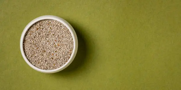 organic white chia seeds rich in omega-3 fatty acids,  a small ceramic bowl on a handmade rag paper with copy space