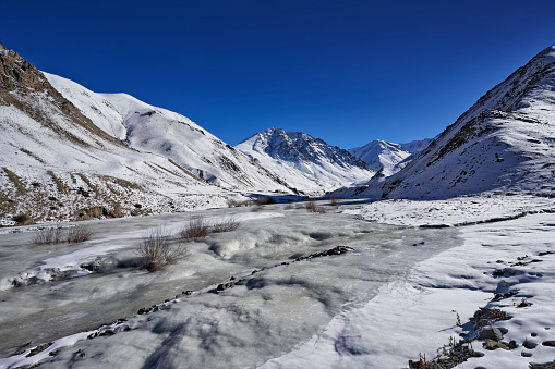 Road to Rumbak Valley and Yarutse, Hemis NP, Ladak, India. River with snow during winter, Himalayas. Mountain landscape in India wild nature. Sunny day with snow in the valley, blue sky with clouds.