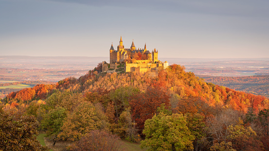 Bisingen, Baden Württemberg, Germany - October, 17th 2020: Majestic Hohenzollern Castle - Burg Hohenzollern hilltop castle panorama in sunrise light in autumn season. Colorful surrounding autumn colored trees around the hill of Burg Hohenzollern. Swabian Jura, Baden Württemberg, Southwest Germany, Germany, Europe.