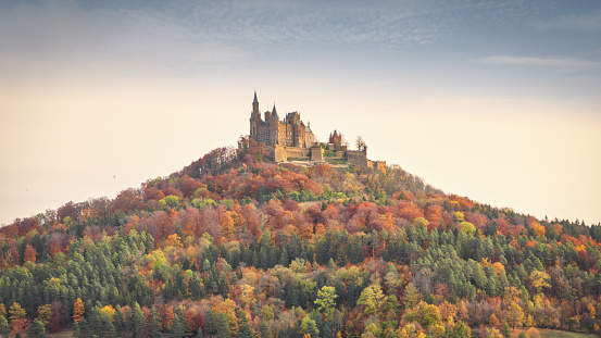Bisingen, Baden Württemberg, Germany - October, 17th 2020: Majestic Hohenzollern Castle - Burg Hohenzollern hilltop castle panorama in moody early morning light during autumn season. Colorful surrounding autumn forest trees around the hill of Burg Hohenzollern. Swabian Jura, Baden Württemberg, Southwest Germany, Germany, Europe.