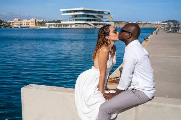Happy couple tourist in Valencia Spain in Mediterranean sea harbor kissing multiethnic couple