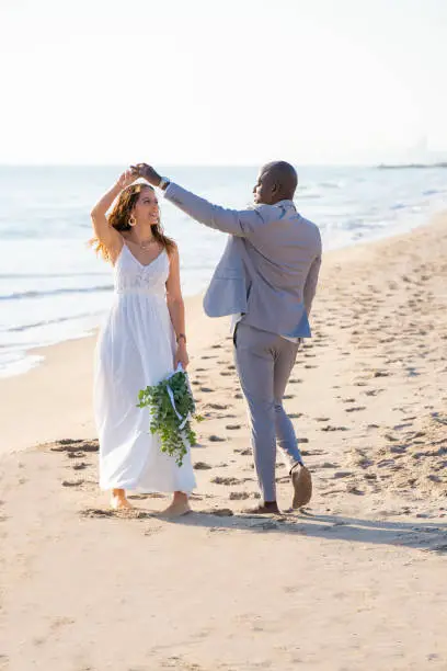Just married honeymoon wedding couple dancing on the beach sand mixed ethnicity happy together