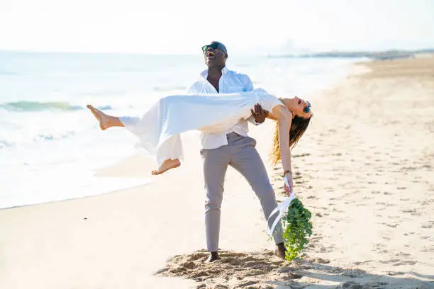 Just married honeymoon wedding couple holding with arms mixed ethnicity on the beach sand happy together