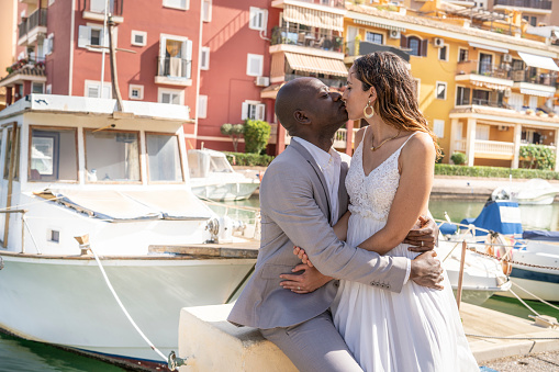Just married honeymoon wedding couple hug kissing mixed ethnicity in a boats marina happy together