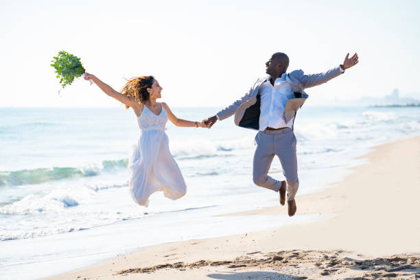 istock Just married honeymoon wedding couple jumping high mixed ethnicity on a beach 1282158230
