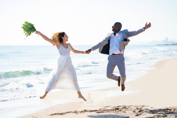 istock Just married honeymoon wedding couple jumping high mixed ethnicity on a beach 1282158260