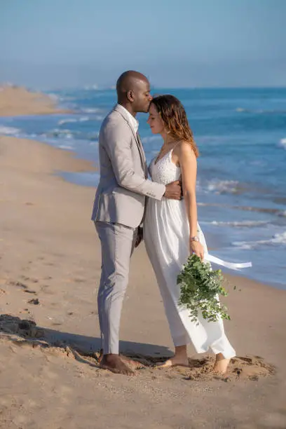 Just married honeymoon wedding couple kissing mixed ethnicity on the beach sand happy together