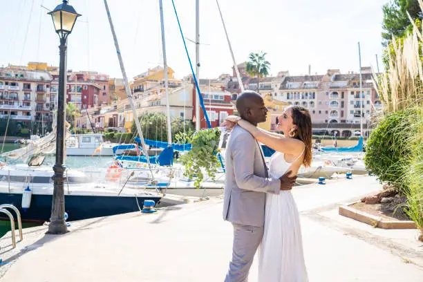 Just married honeymoon wedding couple hug mixed ethnicity in a boats marina happy together