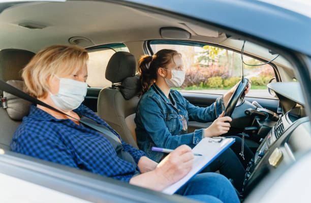 Teenager having driving lesson with female instructor during Covid 19 A teenage girl with protective mask sitting behind the steering wheel of a car and listening to her mothers instructions as she drives. driving test photos stock pictures, royalty-free photos & images