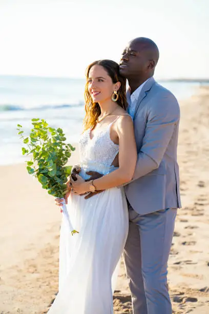 Just married honeymoon wedding couple hug mixed ethnicity on the beach sand happy together