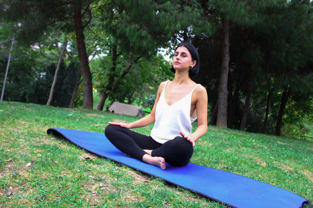 woman doing yoga in cross-legged position in the park - zen like nature breathing exercise sitting imagens e fotografias de stock