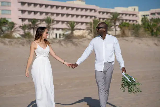 Just married honeymoon wedding walking on beach sand couple mixed ethnicity happy together
