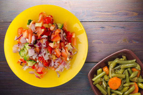 vegan food top view. salad from vegetables pepper, tomato, onions, broccoli on yellow plate. vegan salad on purple wooden background
