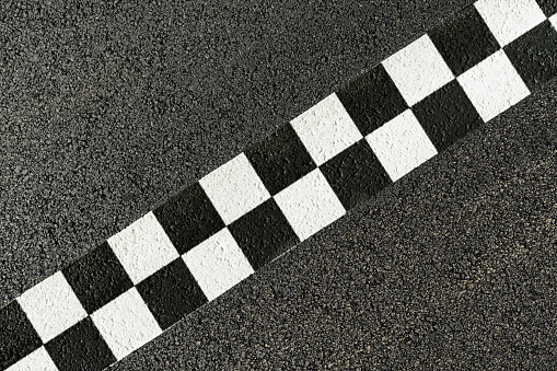 Directly above a freshly painted black and white checkered finish line on a newly paved asphalt race course.