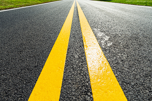 Low above a freshly painted double yellow lane markers on a newly paved asphalt road that vanish in the distance.