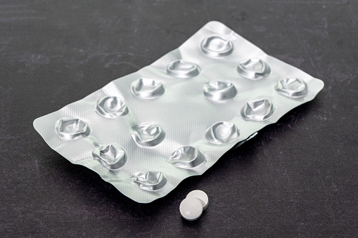 An empty tablet blister pack with just two tablets left  highlighting cost and dependance of medications- plain background