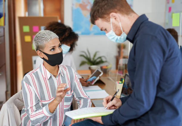 istock Multiracial people working in office with new measures for coronavirus while wearing protective face mask - Coworking, business and technology 1282163620