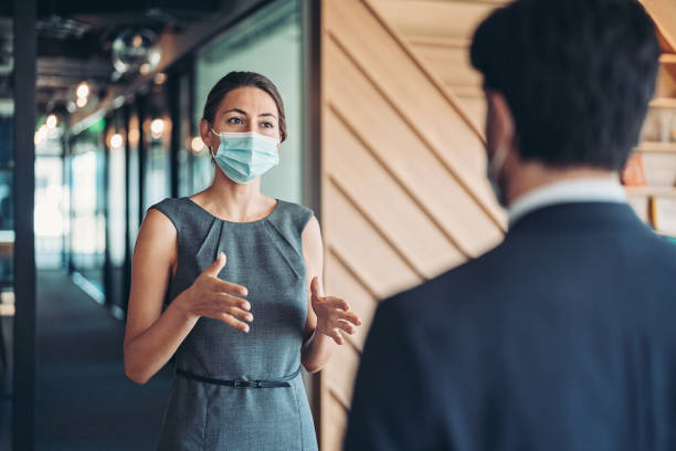 Talking form a safe distance Businesswoman, wearing a mask, standing at distance and talking to a colleague talking two people business talk business stock pictures, royalty-free photos & images