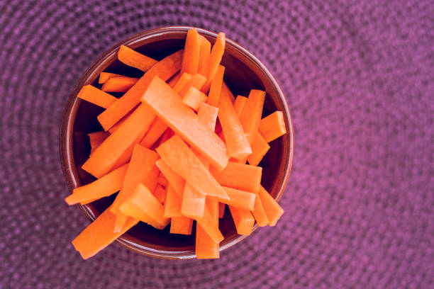 Chopped carrots in a bowl on a plate against a purple background, creative color editing with added grain