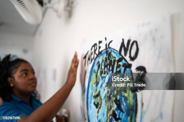 Student fixing in the wall a poster about environmental issues - There is no planet B