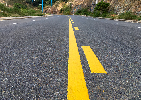 Low angle view of asphalt road with a yellow marking leaving afar