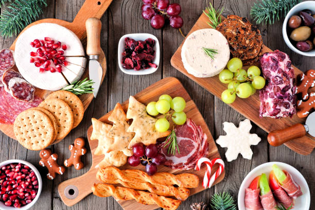 Christmas theme charcuterie top view table scene against dark wood Christmas theme charcuterie table scene against a dark wood background. Assortment of cheese and meat appetizers. Top view. appetizer stock pictures, royalty-free photos & images