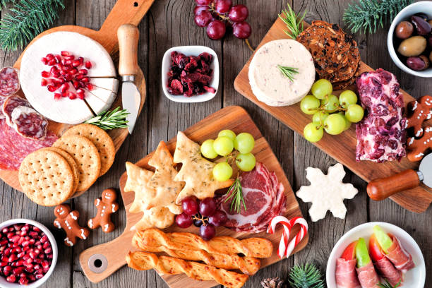 Christmas theme charcuterie top view table scene against dark wood Christmas theme charcuterie table scene against a dark wood background. Assortment of cheese and meat appetizers. Top view. prosciutto brie stock pictures, royalty-free photos & images