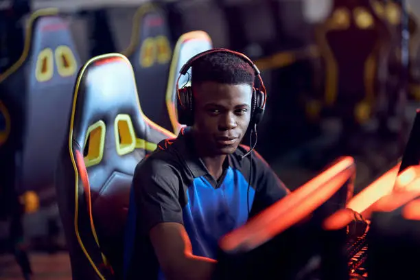 Photo of Portrait of a happy african guy, professional gamer wearing headphones looking at camera and smiling while participating in eSport tournament