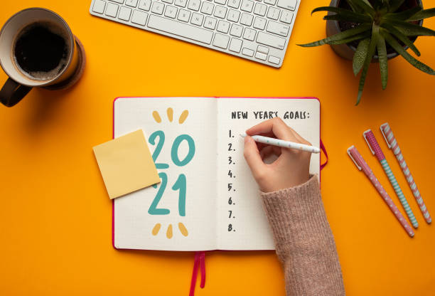 Woman writing goals in a 2021 new year notebook Stock photo of woman writing goals in a 2021 new year notebook on yellow background 2021 photos stock pictures, royalty-free photos & images