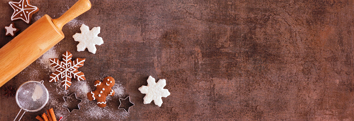 Christmas baking corner border with gingerbread cookies. Above view over a dark stone banner background with copy space. Holiday baking concept.