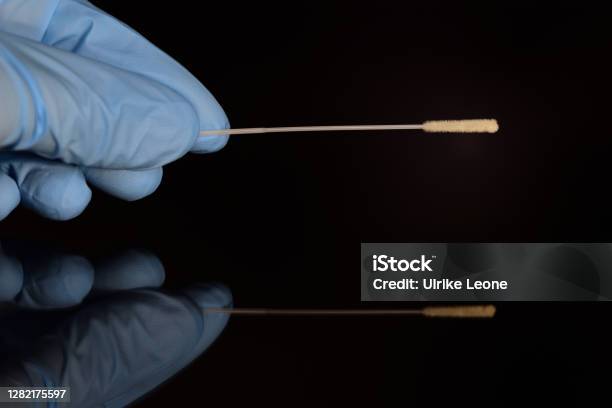 A Hand Wearing A Blue Disposable Glove Holds A Swab For A Swab In Order To Carry Out A Corona Test The Background Is Dark And The Hand Is Reflected Stock Photo - Download Image Now