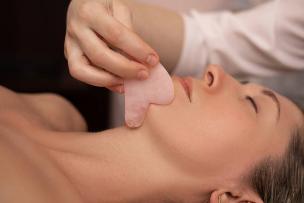 mulher jovem e bonita durante a massagem tradicional chinesa - gua sha. foto de close-up. tratamento de beleza em salão spa - spooning - fotografias e filmes do acervo