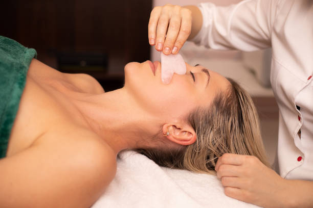 jeune et belle femme pendant le massage traditionnel chinois - gua sha. photo de plan rapproché. traitement de beauté dans le salon spa. soins de la peau anti-âge - massaging spa treatment stone massage therapist photos et images de collection