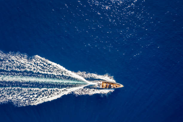 Aerial top down view of a motorboat traveling over blue sea Aerial top down view of a motorboat traveling over blue sea wake water stock pictures, royalty-free photos & images