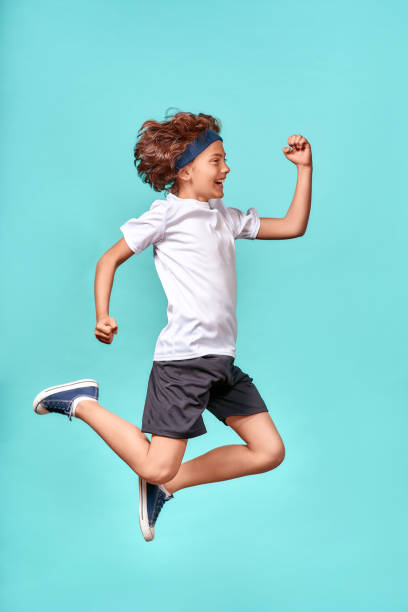 in motion. full-length vertical shot of a happy, full of energy teenage boy jumping isolated over blue background - carefree joy children only pre adolescent child imagens e fotografias de stock