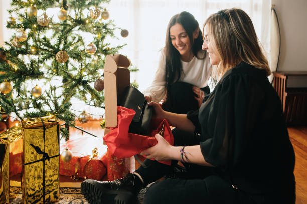istock Two women opening a Christmas present by a Christmas tree 1282189681