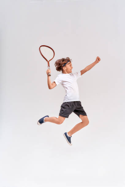 scatto a figura intera di un adolescente che salta con una racchetta da tennis isolata su sfondo grigio, colpo in studio - tennis child teenager childhood foto e immagini stock