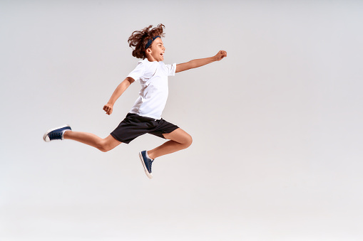 freedom, motion and happiness concept - happy smiling young boy jumping in air over grey background